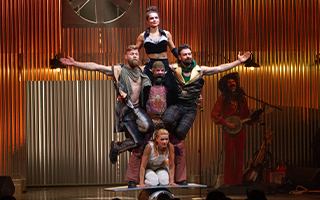 Photo from the performance of 'Animal' by Alfonse Circus. Five performers on a stage showcase a lift while one person behind plays the banjo.