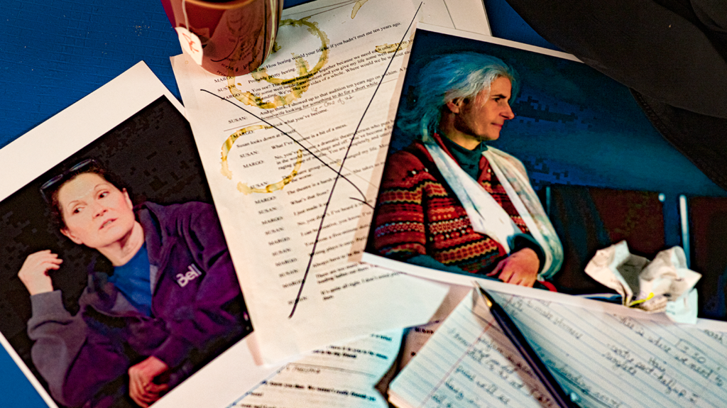 On a table lies a photo of a woman in a hoodie, a script with coffee stains and a mug atop it, and a photo of a woman with her arm in a sling.