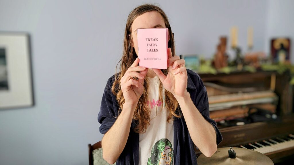 Photo of Arden Rogalsky holding their pink book titled, 'FREAK FAIRY TALES.' 