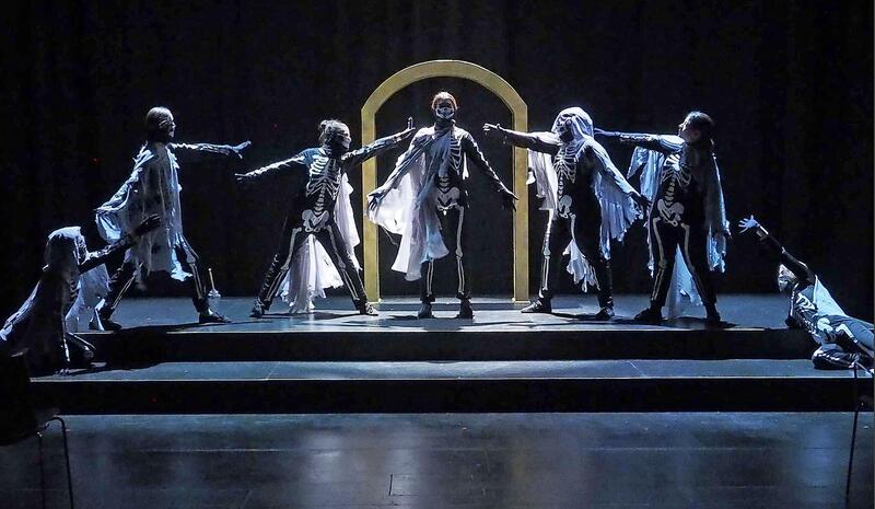 Seven performers dressed as skeletons on a dimly lit stage. It is the cast of Everybody produced by DAN School of Drama and Music.