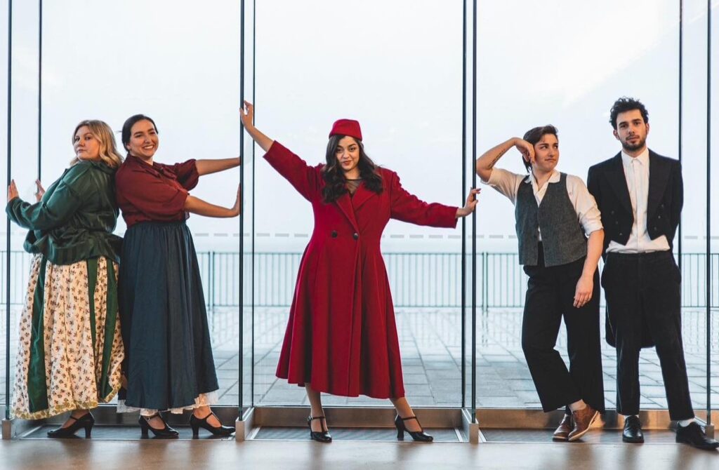 The cast of Queen's Musical Theatre 'Funny Girl' posing against a large window.