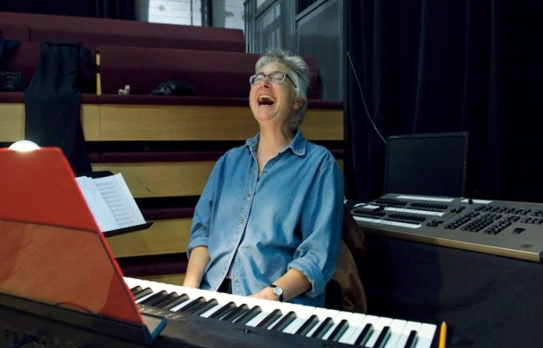 Photo of Leslie Arden sitting at a piano and laughing.