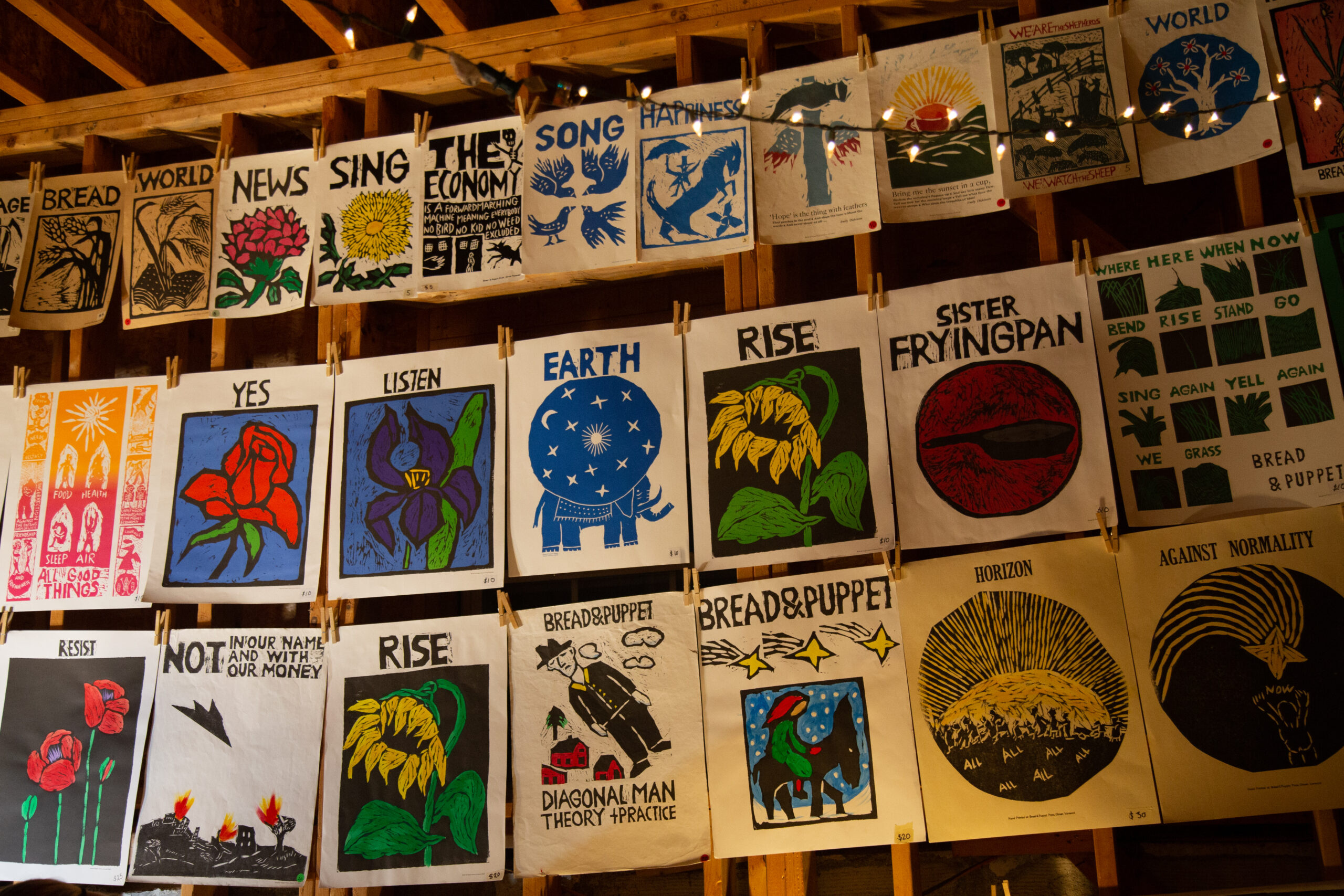 Many posters for Bread and Puppet Theater's 'Inflammatory Earthling Rants' line a wall in three rows.