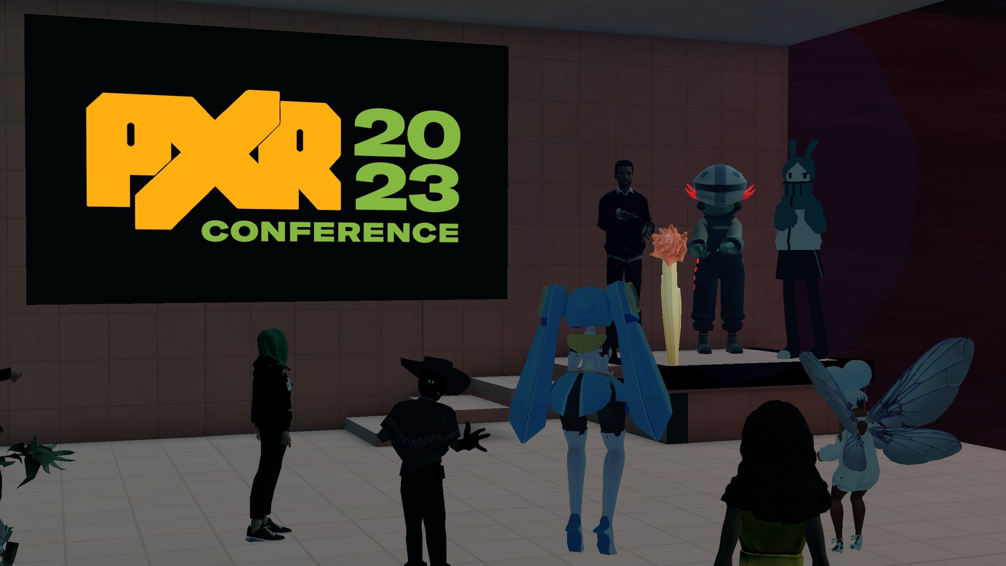 Attendees of PXR Conference 2023 attending in Virtual Reality. There are multiple avatars looking at a screen that reads "PXR Conference 2023"