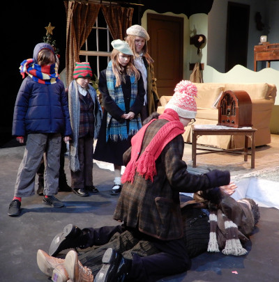 Performers in Domino Theatre's production of 'A Christmas Story'. Four children are seen standing watching an interaction where one child is pin to the ground and another child kneels overtop of them.