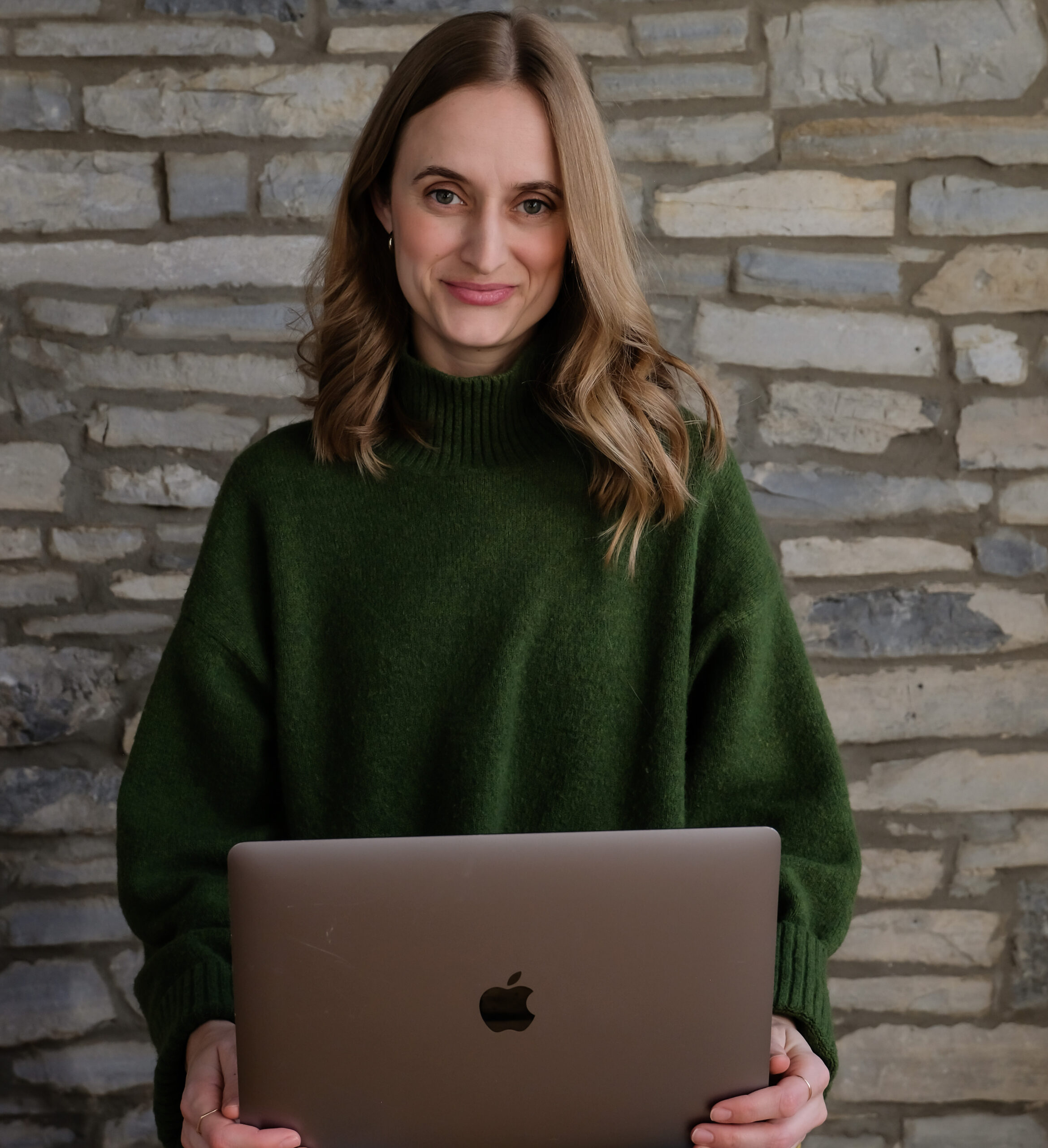 Image of Sophia Fabiilli sitting against a rock wall holding a laptop.