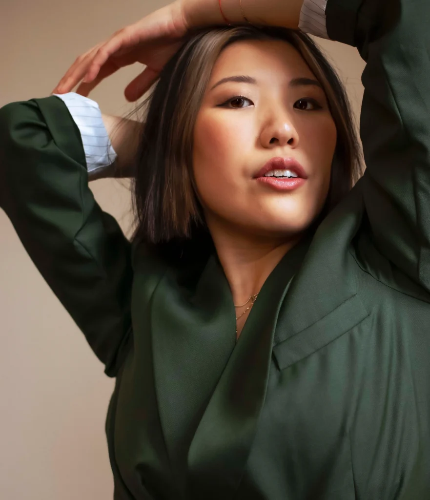 Photo of Stephanie Fung. They wear a green jacket and have their arms above their head. 