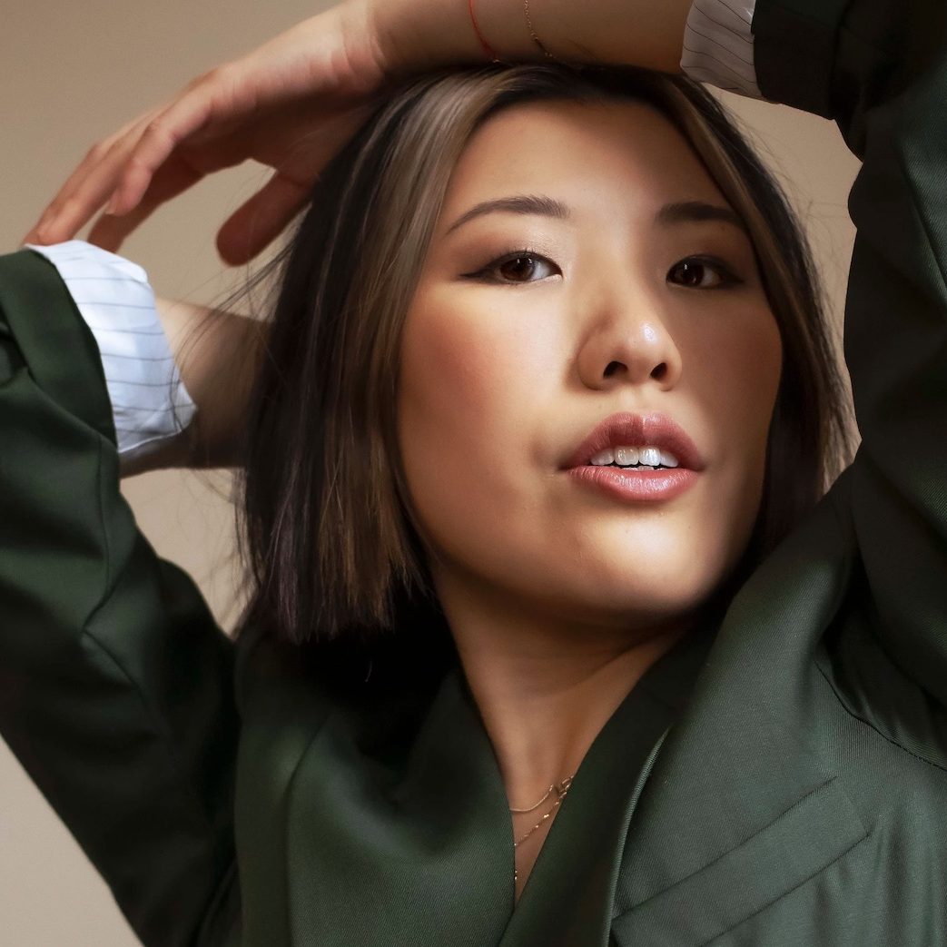 Photo of Stephanie Fung. They wear a green jacket and have their arms above their head.