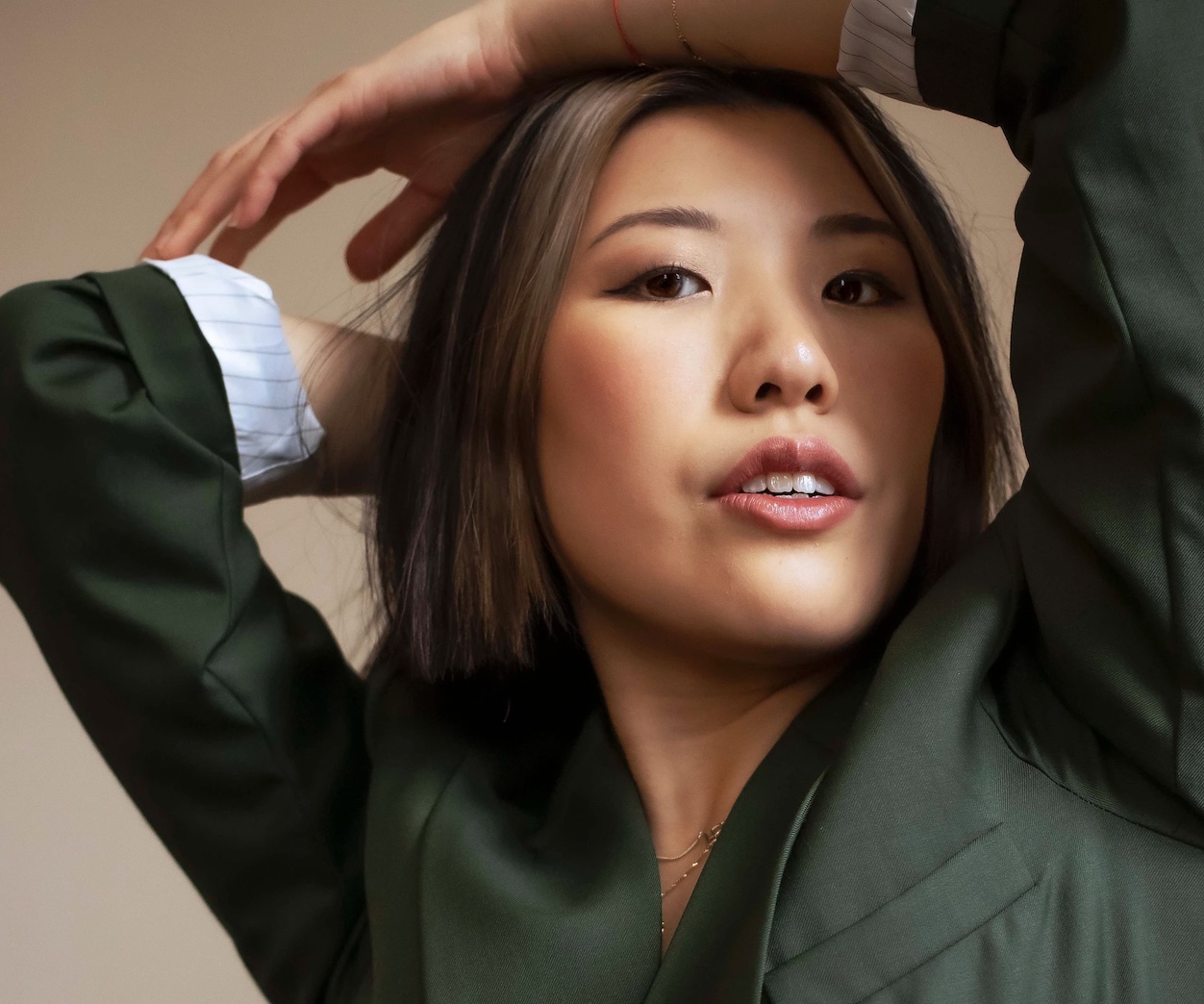 Photo of Stephanie Fung. They wear a green jacket and have their arms above their head.