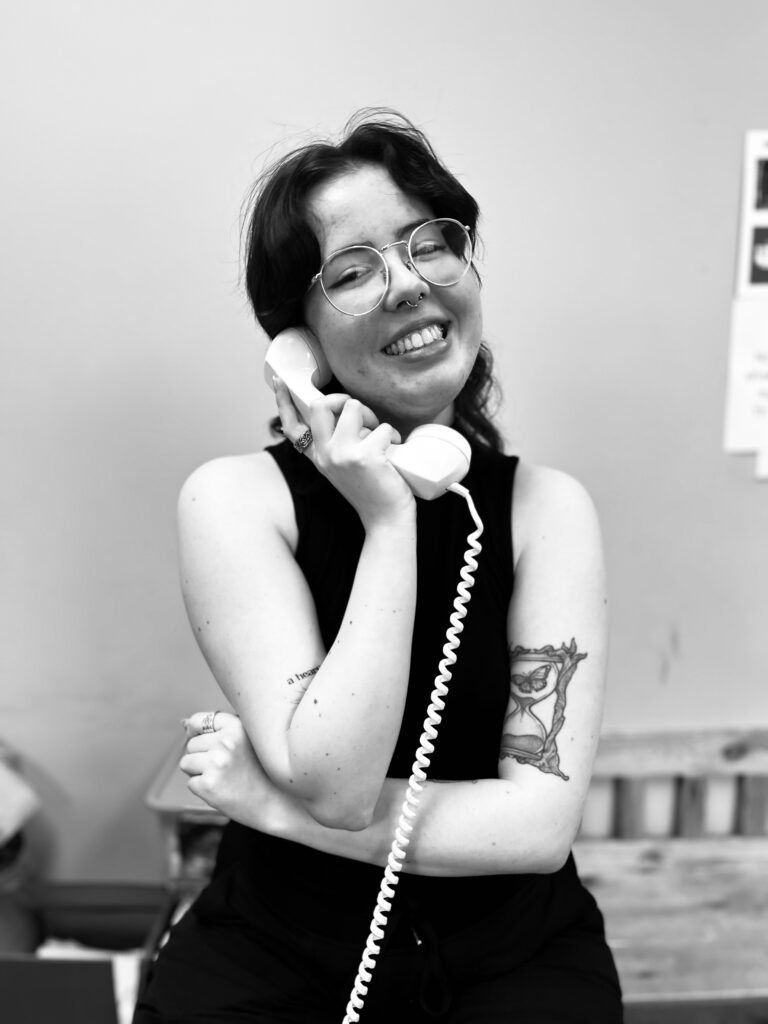 A black and white image of Shay O'Brien holding a rotary phone and smiling. 