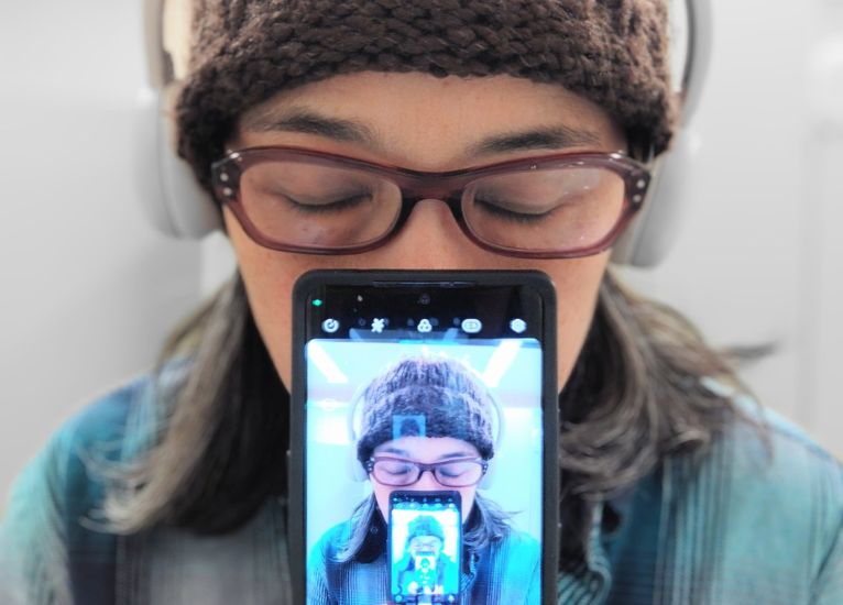 Image of a person with a phone in front of them. Phone shows a picture of them with a phone in front of them. That phone shows a picture of them with a phone in front of them, so on and so forth.
