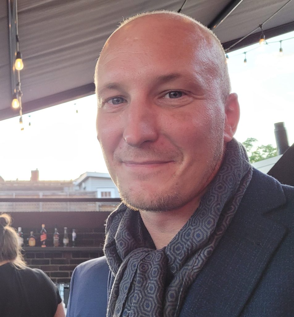 Headshot of Michael Wheeler outside with a scarf and blazer on. 