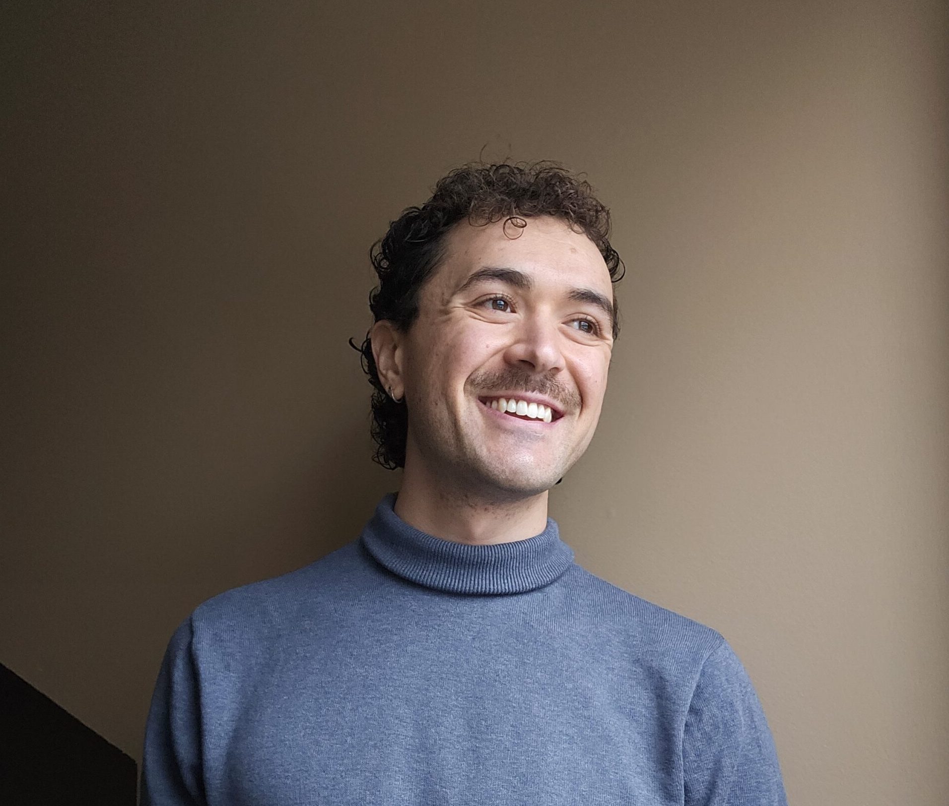 Image of Jeff McGilton. He wears a blue turtleneck and smiles looking off to the side.