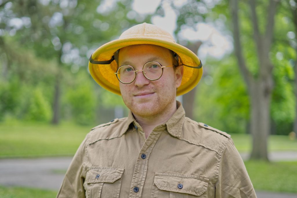 Jesse Gazic outside, wearing a yellow cap, glasses, and beige shirt.