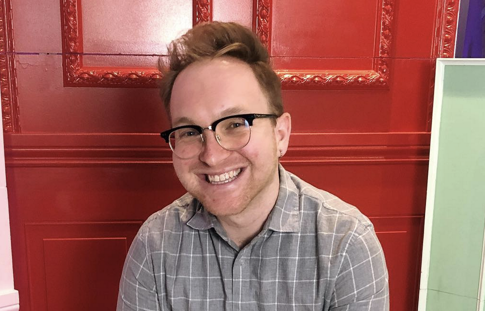 Photo of Jesse Gazic. He is smiling, against a red, pink, and green wall.