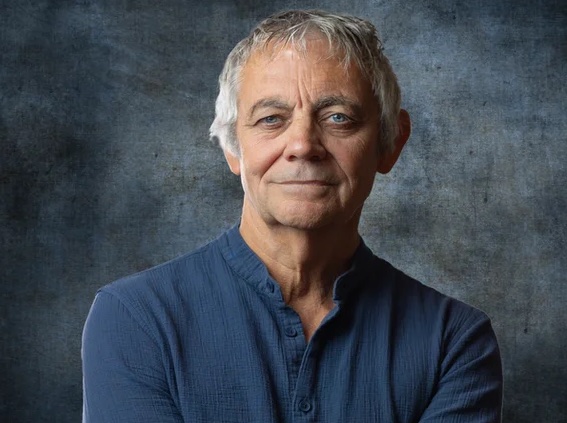 Headshot of Richard Willis. He wears a blue shirt and stands in front of a grey-blue background.