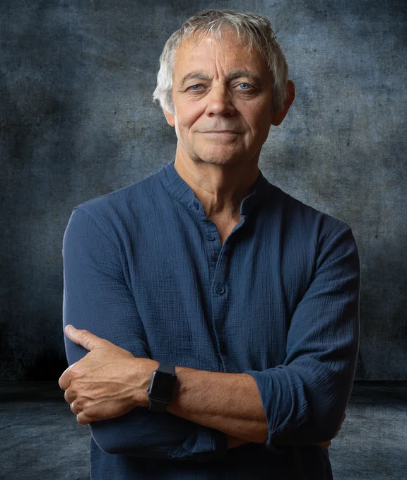 Headshot of Richard Willis. He wears a blue shirt and stands in front of a grey-blue background. 