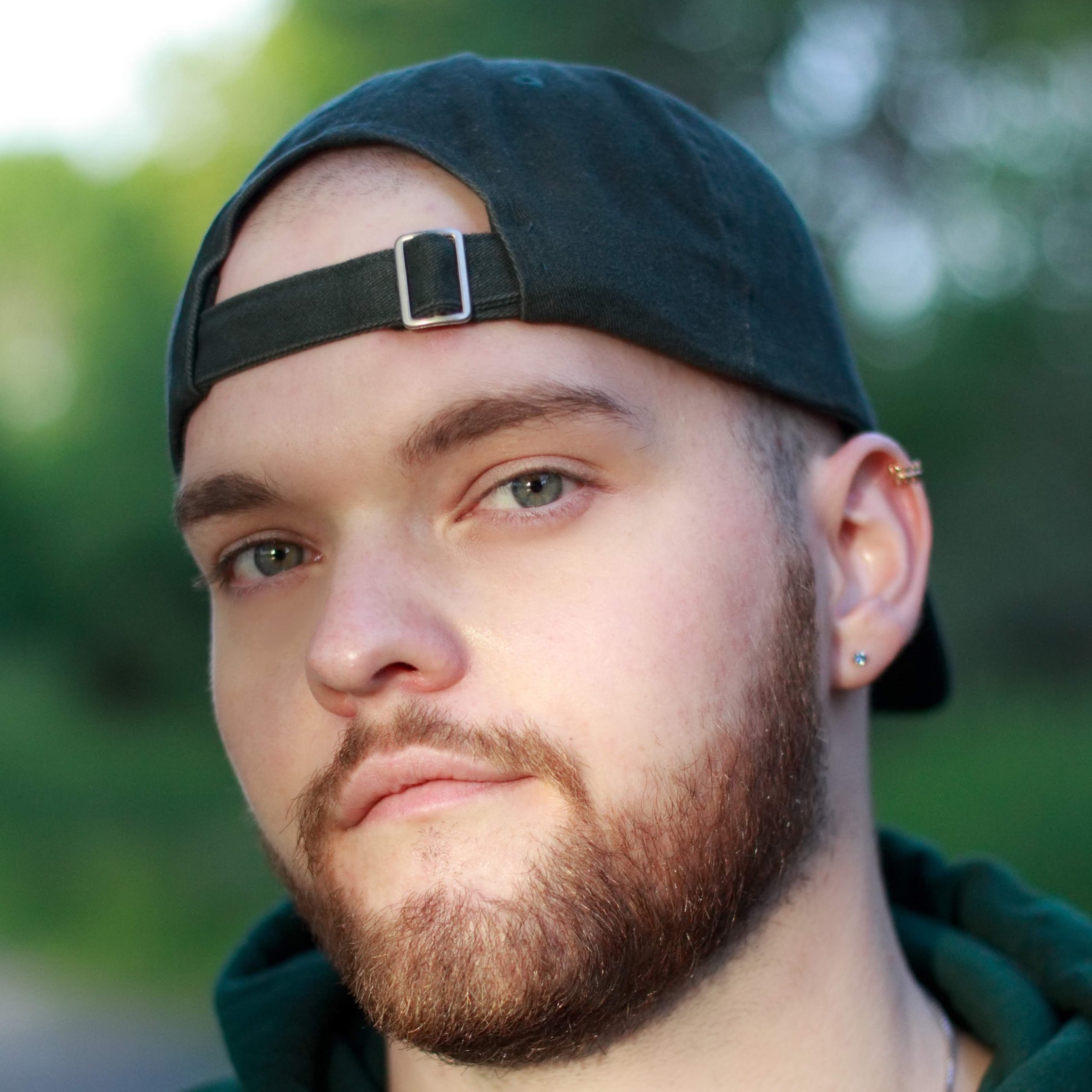 Headshot of B.C. Gorrie. He is outside, wearing a black hoodie and black baseball cap backwards. He looks into the camera.