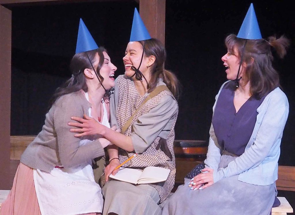 Three actors. They laugh with each other and are wearing party hats.