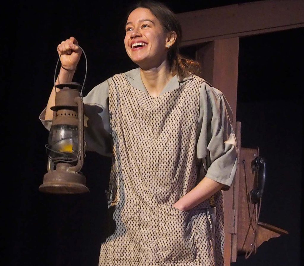 An actor holds a lantern and smiles into the distance.