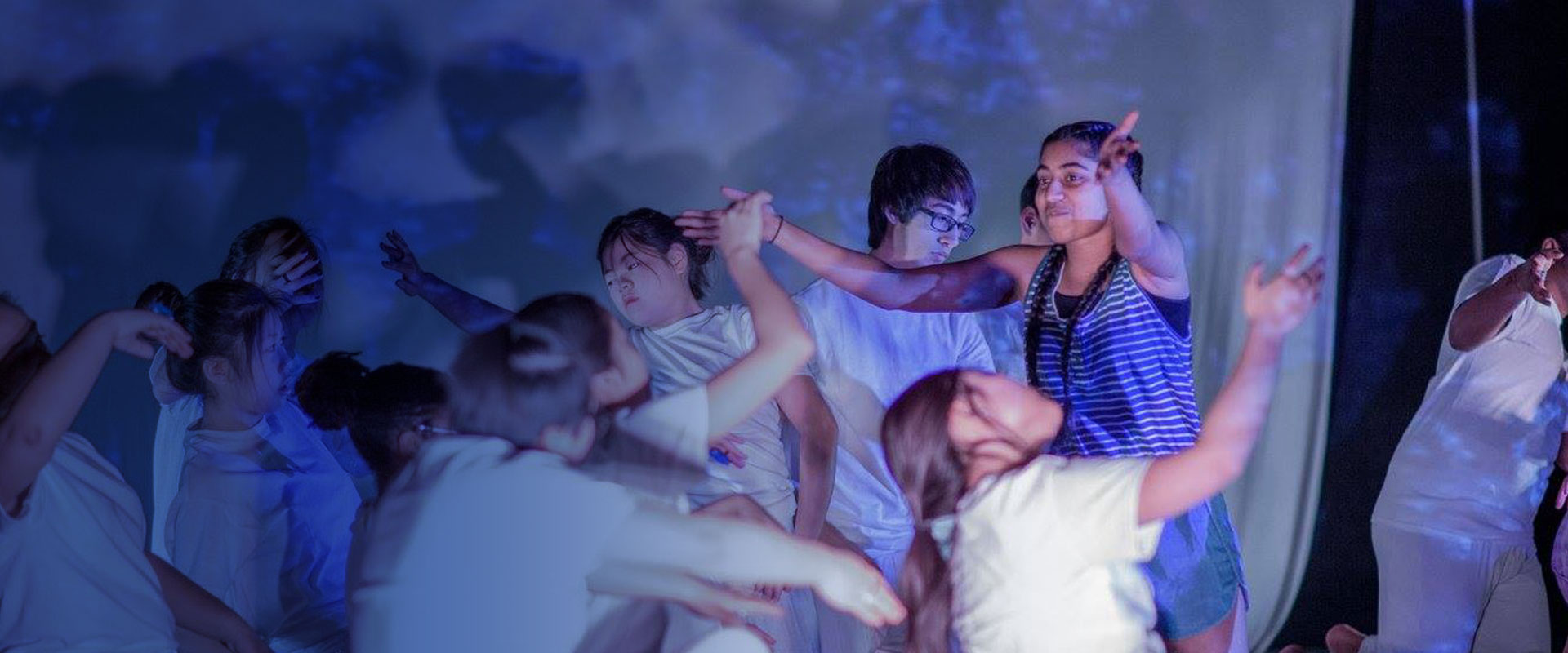Image of high school students performing. The lights are low and they are moving across a stage.