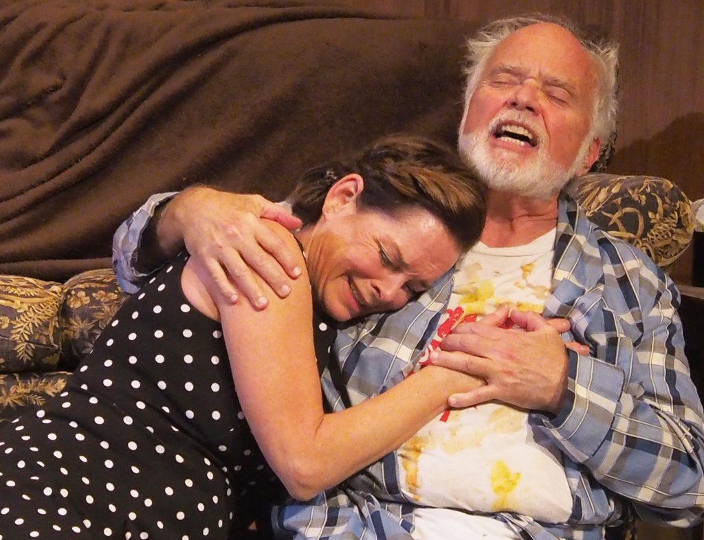 Two people sit hugging on a couch.