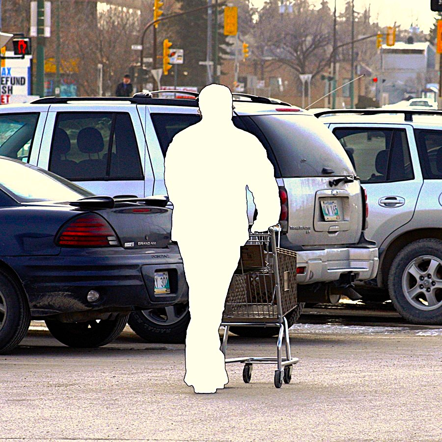 A white figure pushes a shopping cart in a parking lot.