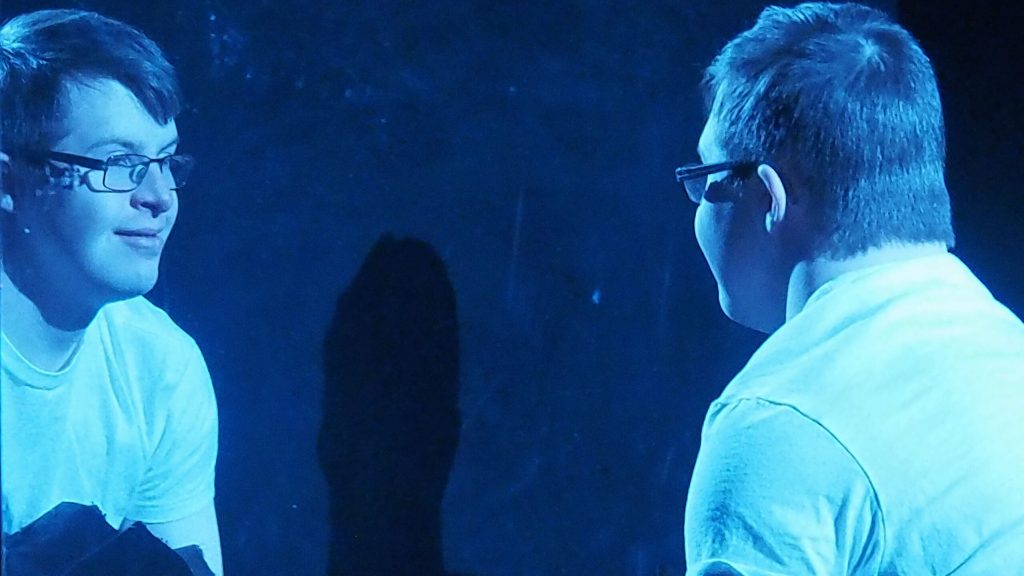 Someone looks in a mirror with blue tinted lighting.