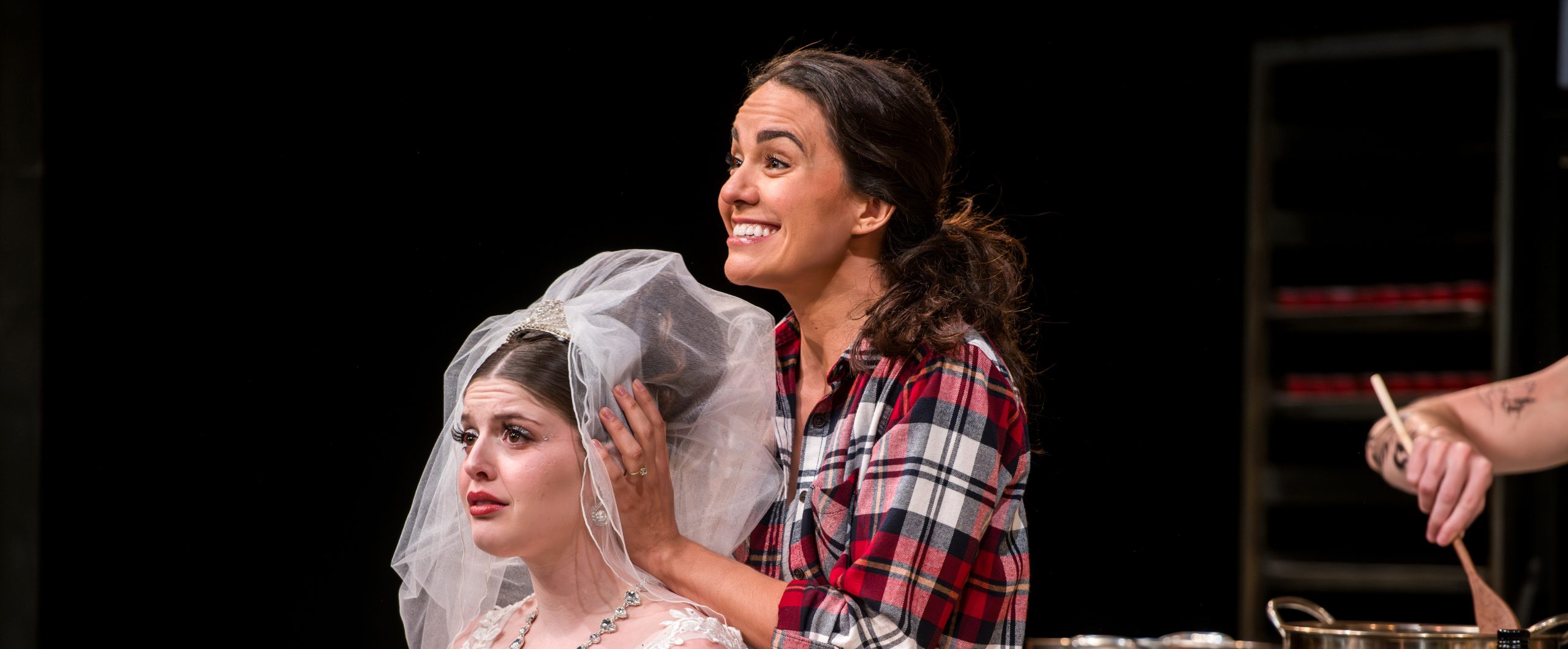 Image of a bride looking worried and her maid of honour smiling happily behind her.