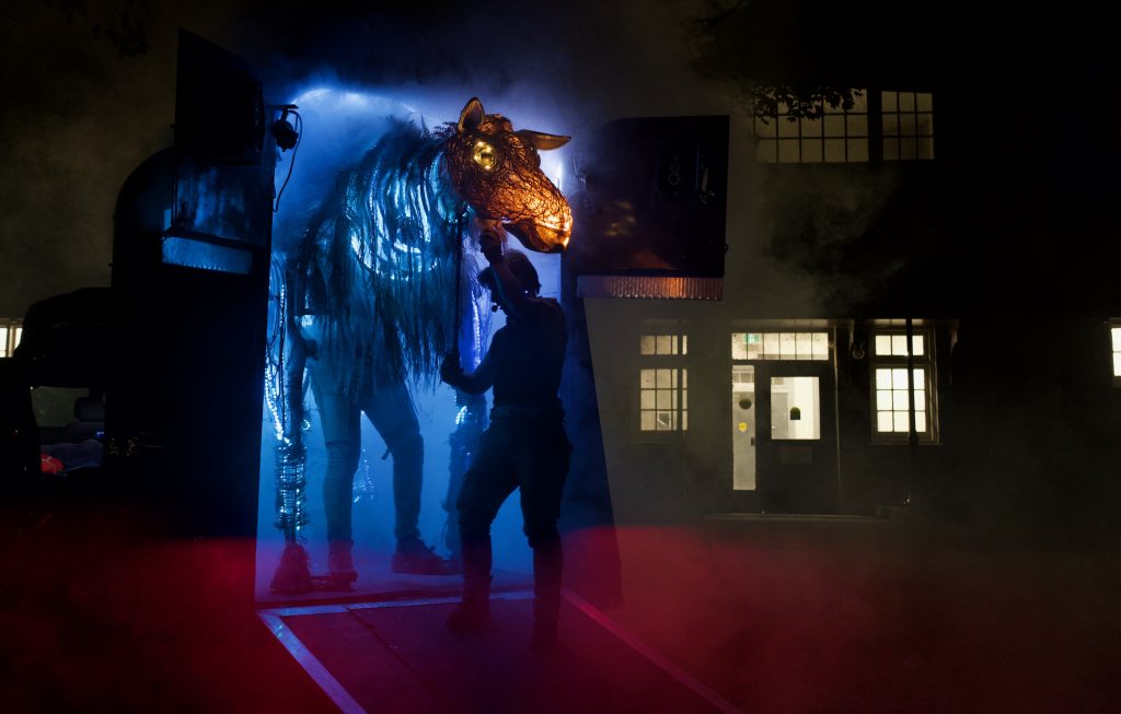 A large puppet moose emerging from a trailer bathed in a magical glow.