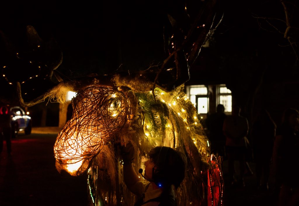 A large puppet moose adorned with twine and lights. 