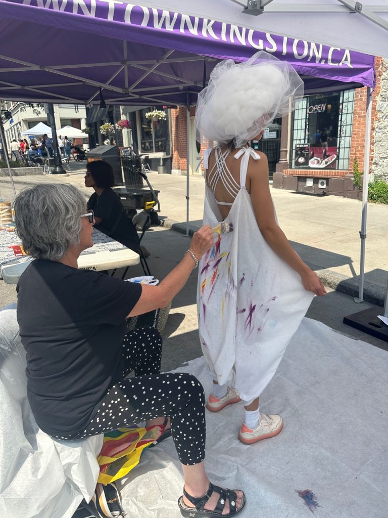 Person painting onto a white dress someone else is wearing.