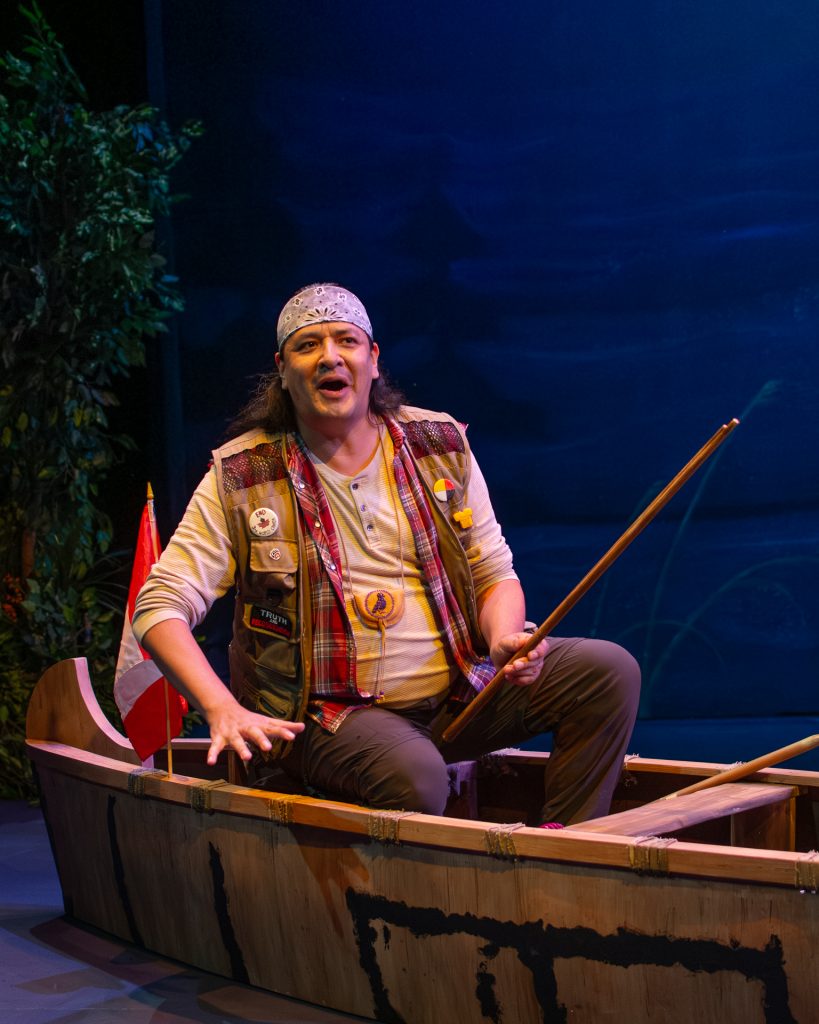A man sits in a stage canoe with a paddle.