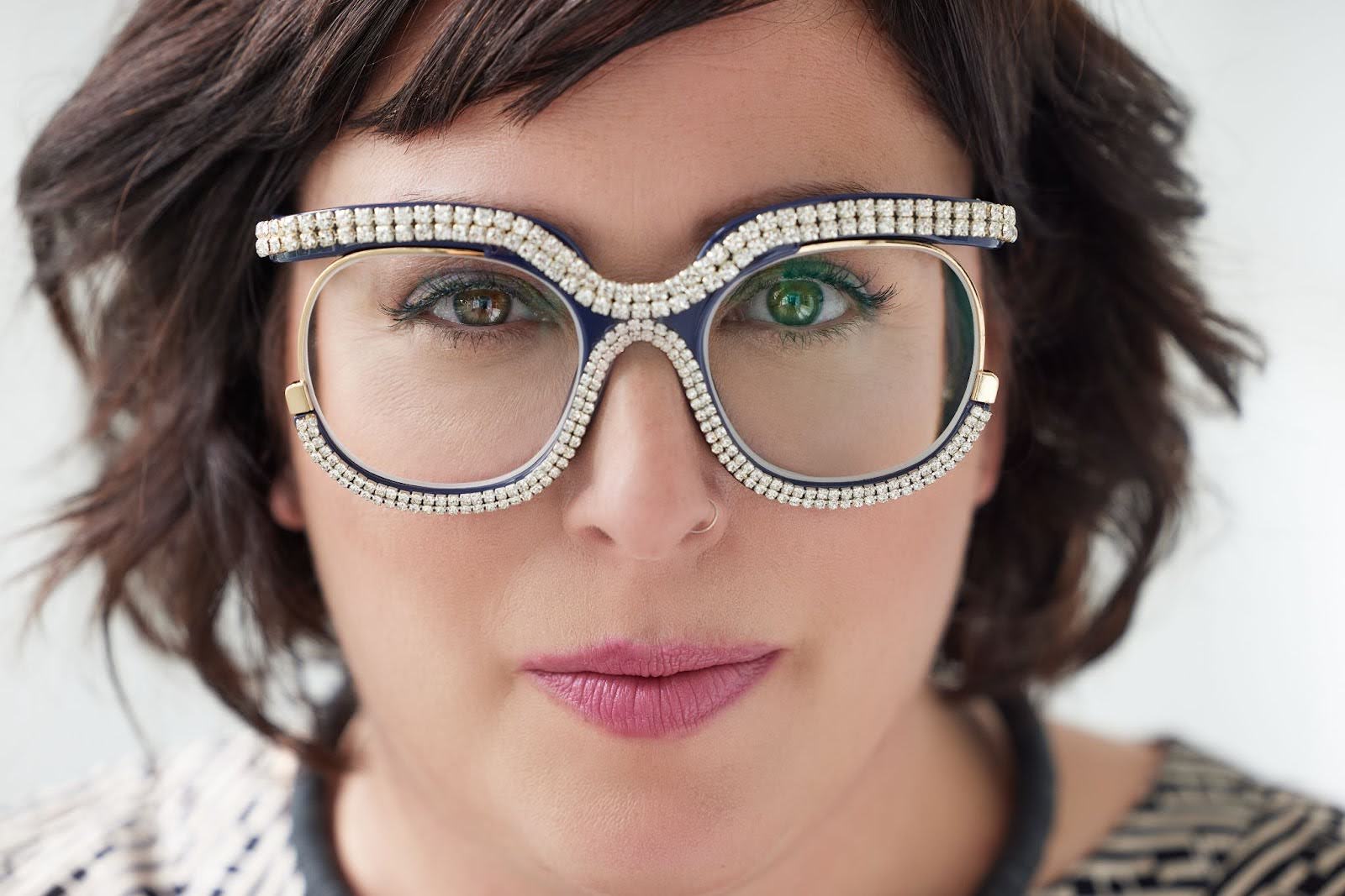 Headshot of Andrea Superstein. She looks a the camera wearing bedazzled glasses.