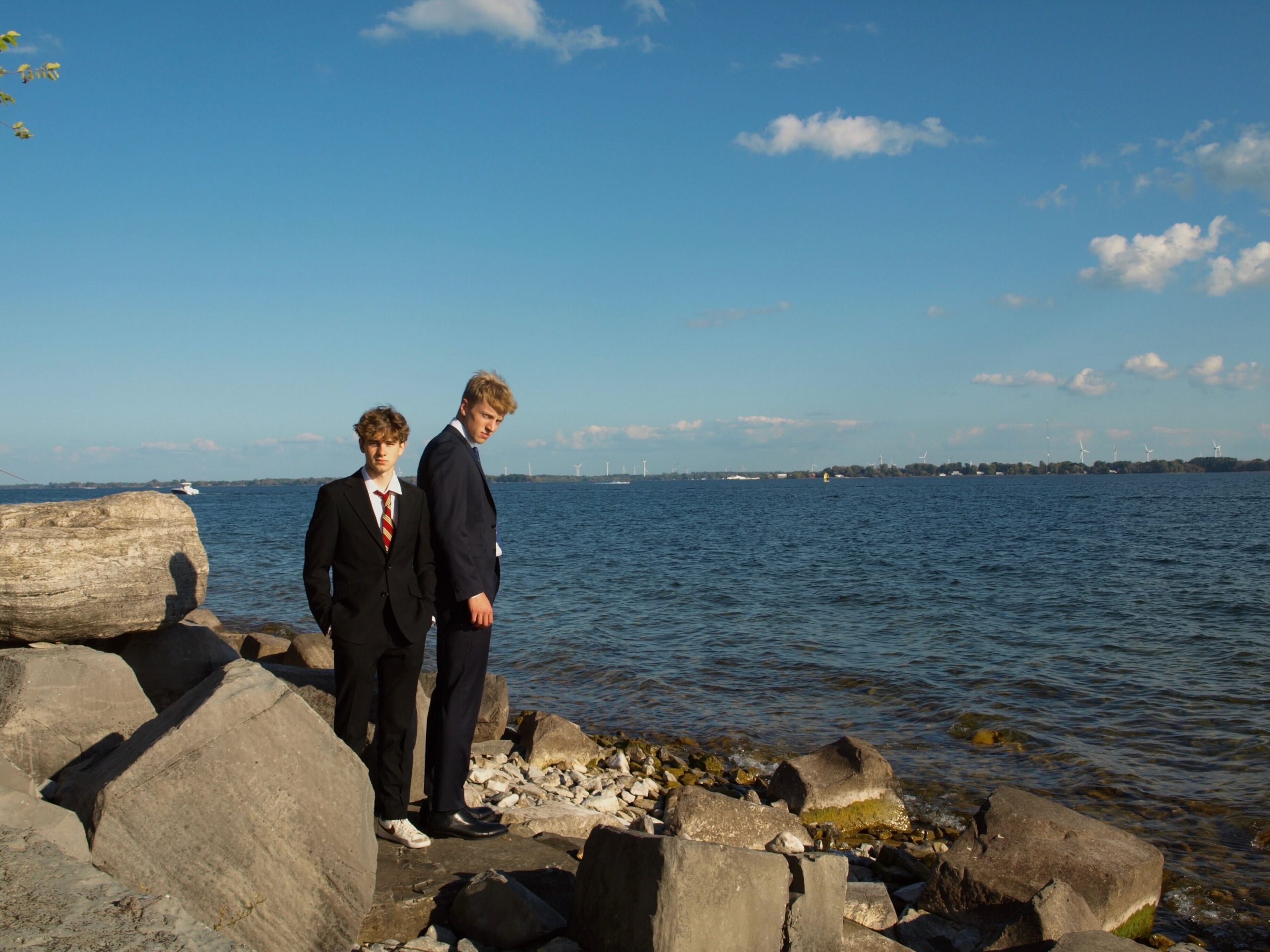 Two young white men in suits standing on a rocky beach.