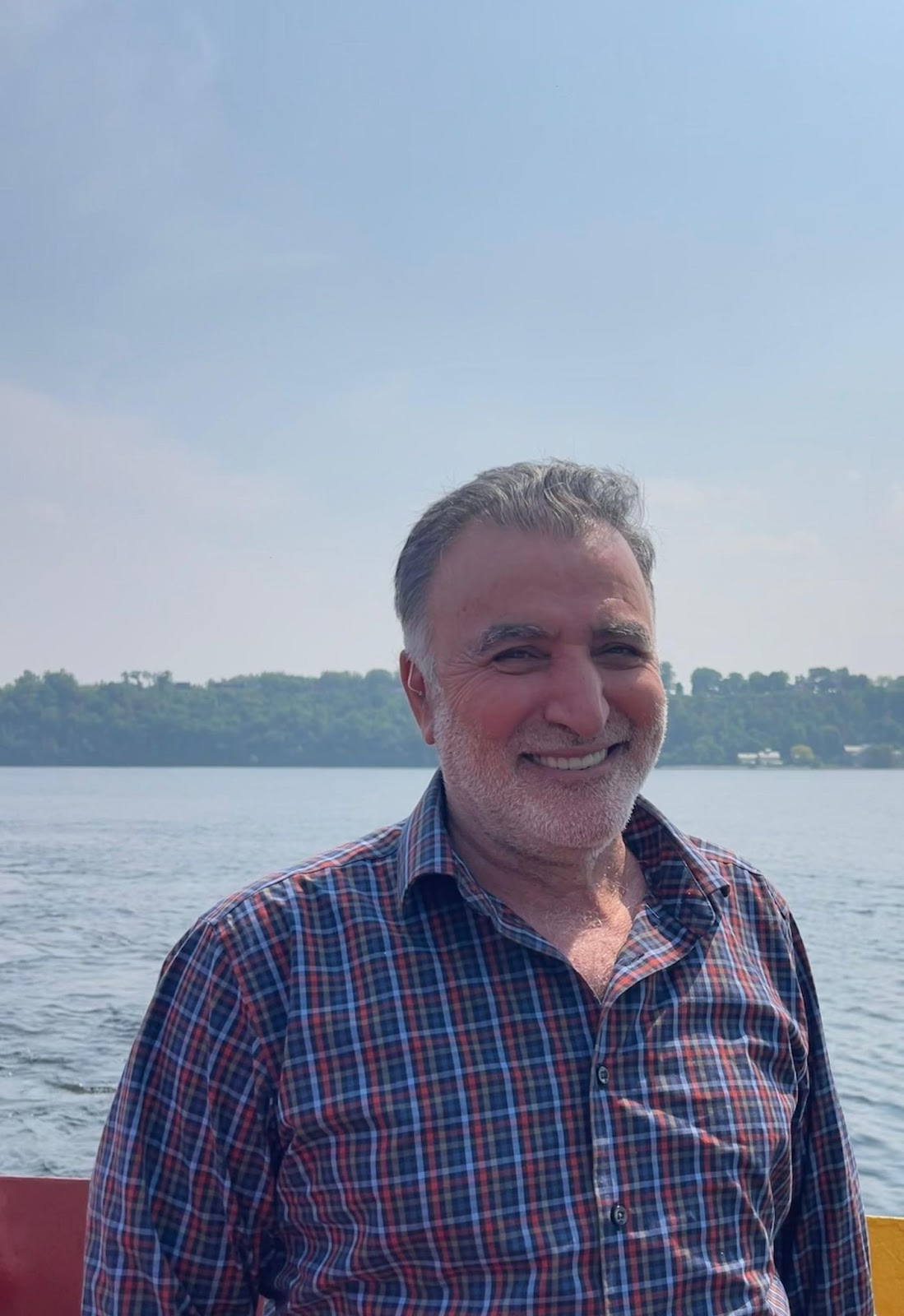 A man with grey hair smiling, backdropped by a large body of water.