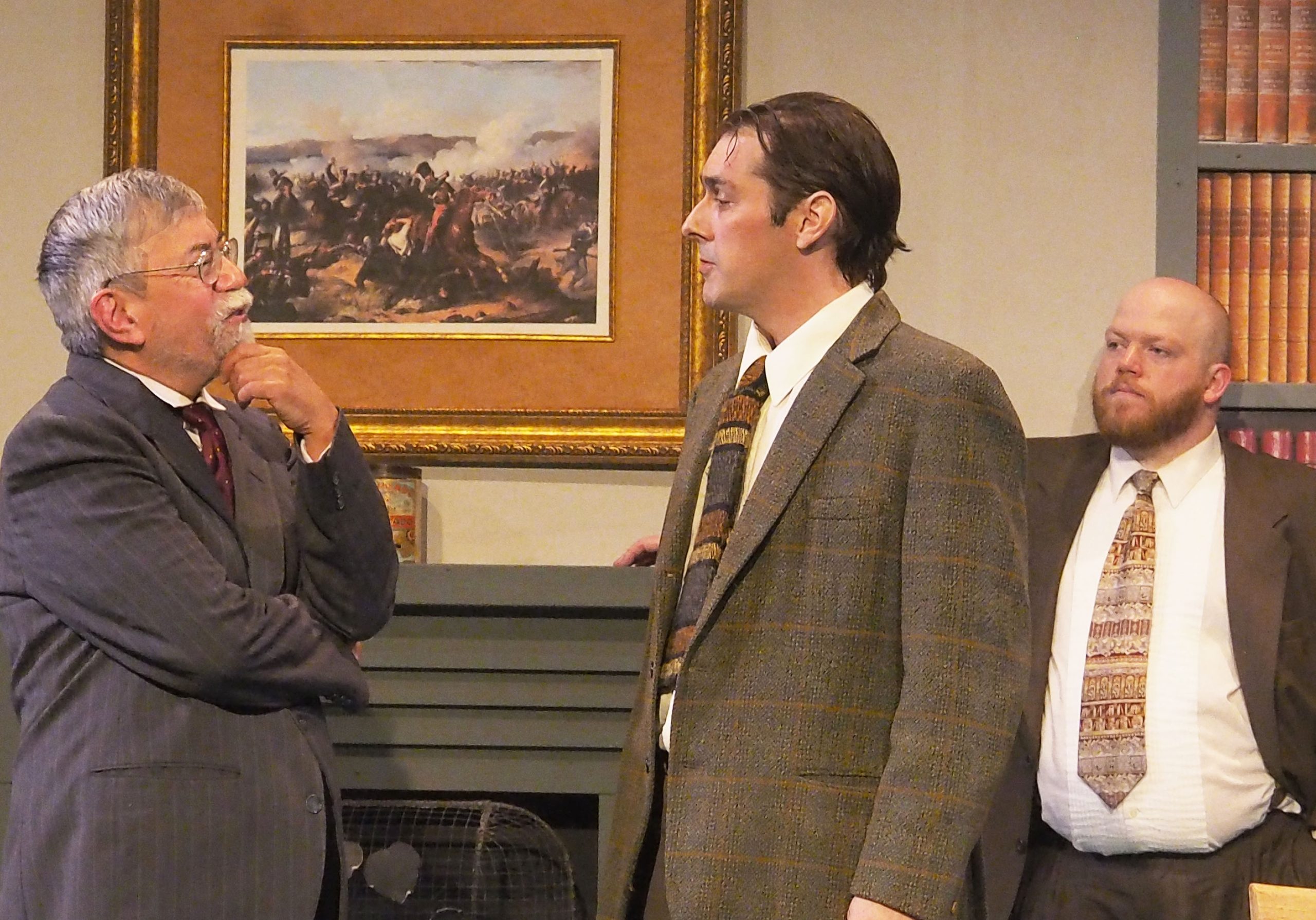 Three performers in Domino Theatre's production of 'Witness for the Prosecution'. Two seemed engaged in a conversation and one seems to observe. They are all dressed in suits.