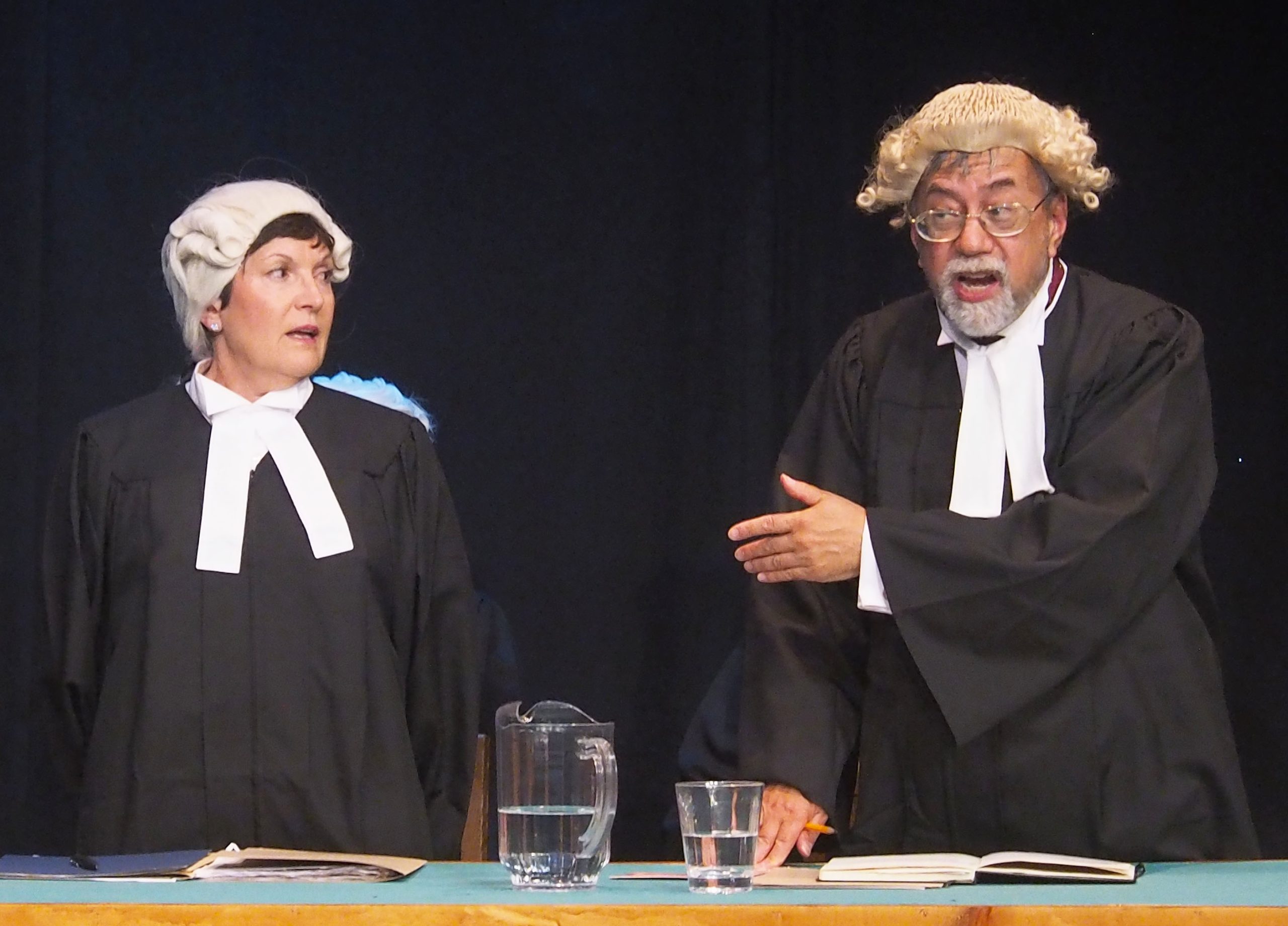 Two performers in Domino Theatre's production of 'Witness for the Prosecution'. Both are dressed as judges and one motions towards the other, looking frustrated.