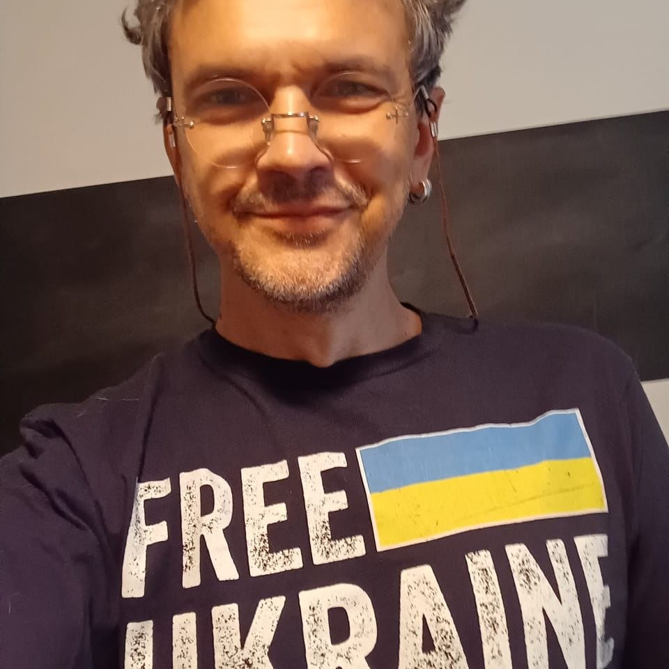 A man with grey hair smiling, wearing a shirt with the Ukrainian flag that says "Free Ukraine"