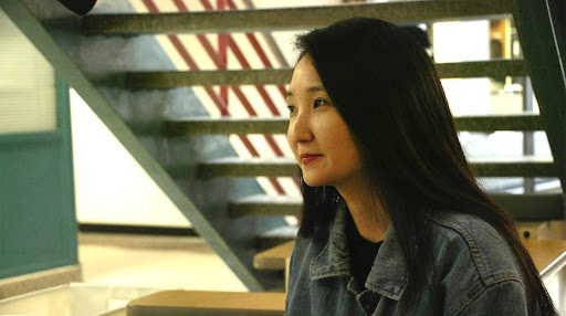 Headshot of Jung-Ah Kim. There is a staircase in the background and the photo is portrait-wise.