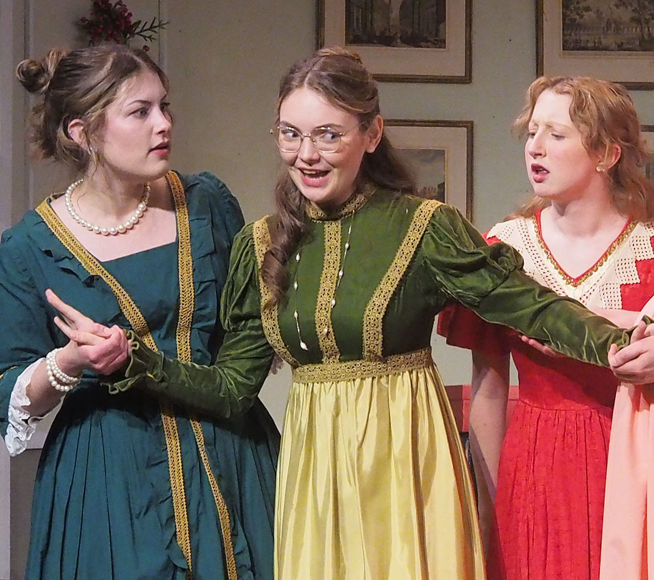Three actors in dresses of 17th-century style. Two actors hold onto the one in the middle. 