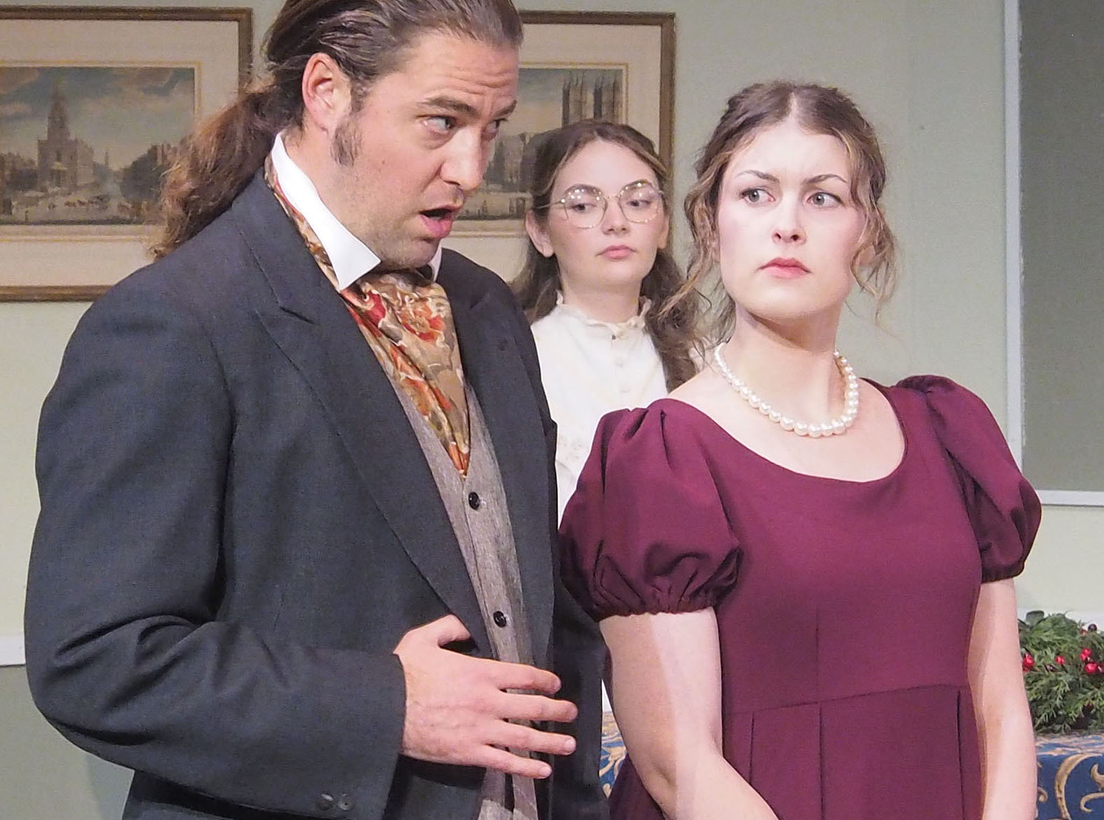Three actors performing. They are all well-dressed and one appears concerned while another speaks. The third appears distracted. 