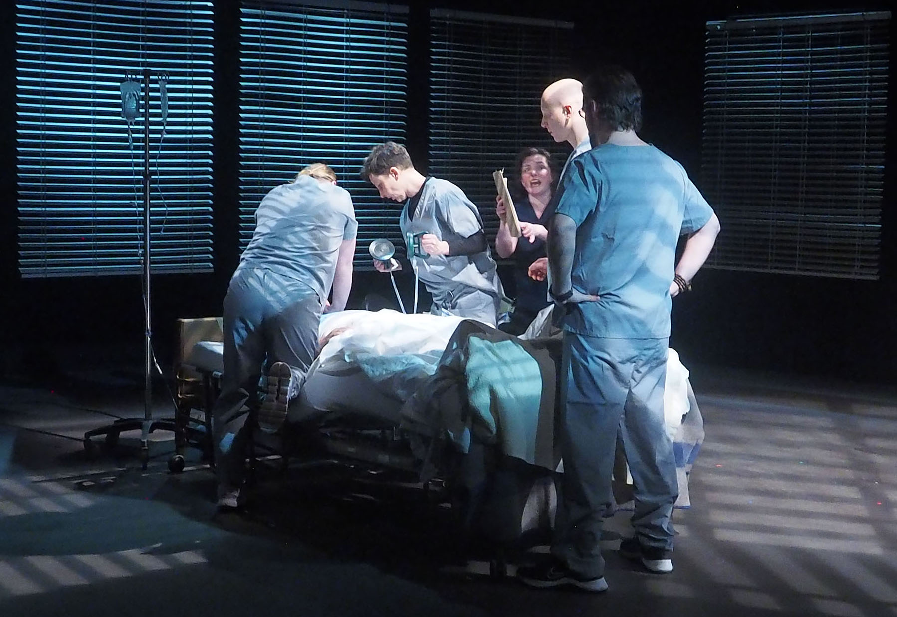 A stage performance where hospital staff is concernedly looking over a patient in their bed. 