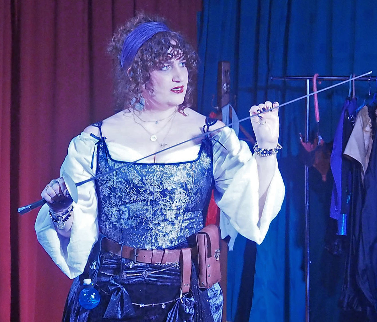 A woman wearing a corset and a belt with loops for gadgets holds a sword.