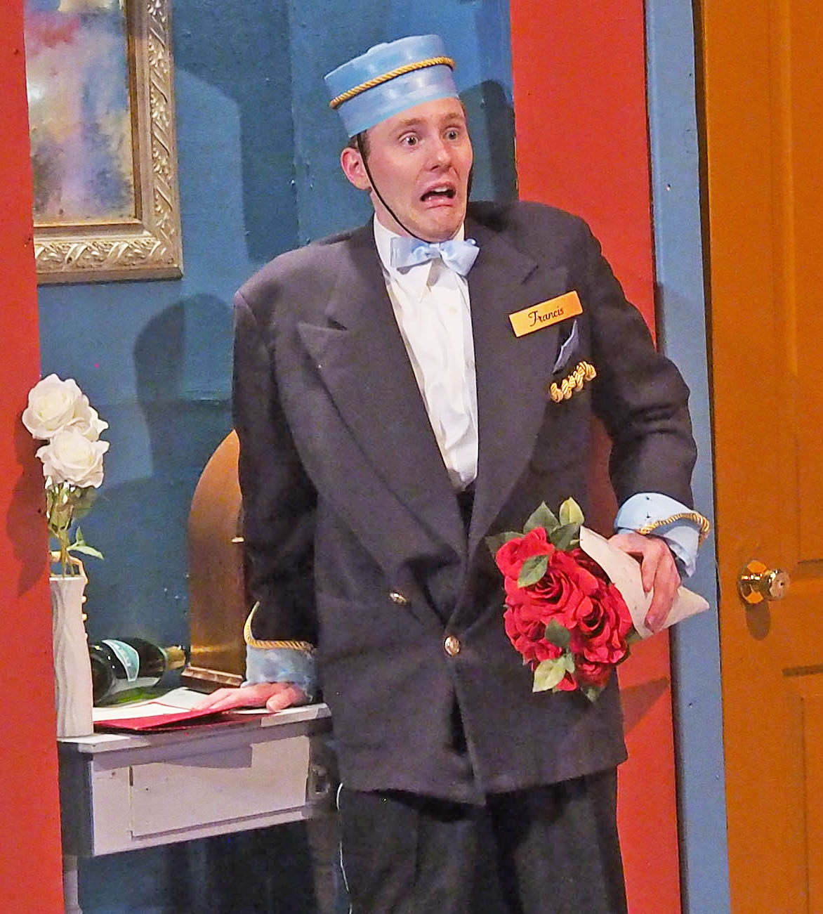 A lobby boy holds a bouquet of roses looking terrified.