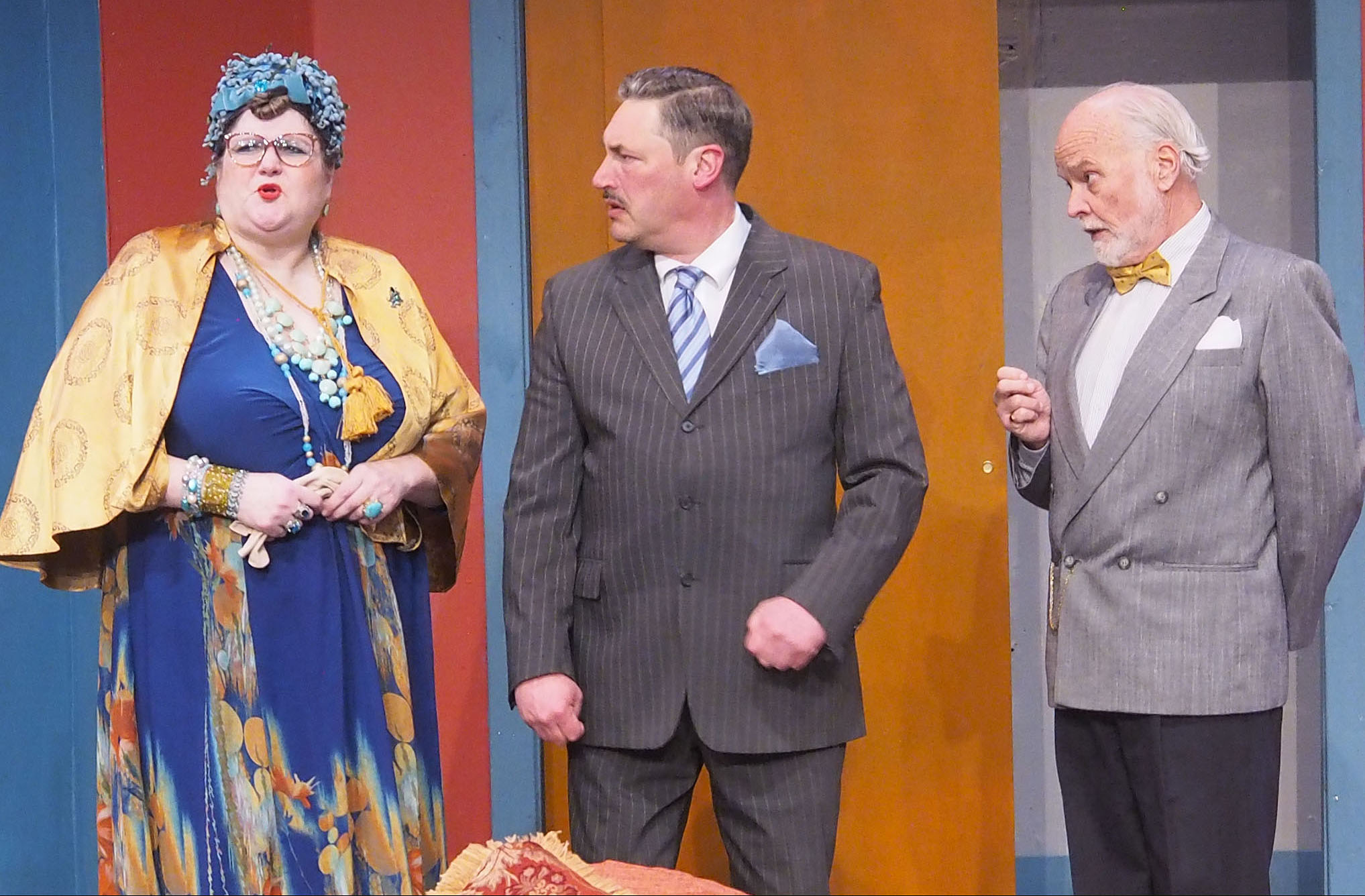 Two men in suits looked worriedly at a woman dressed in high-end fashion and a lot of jewelry.