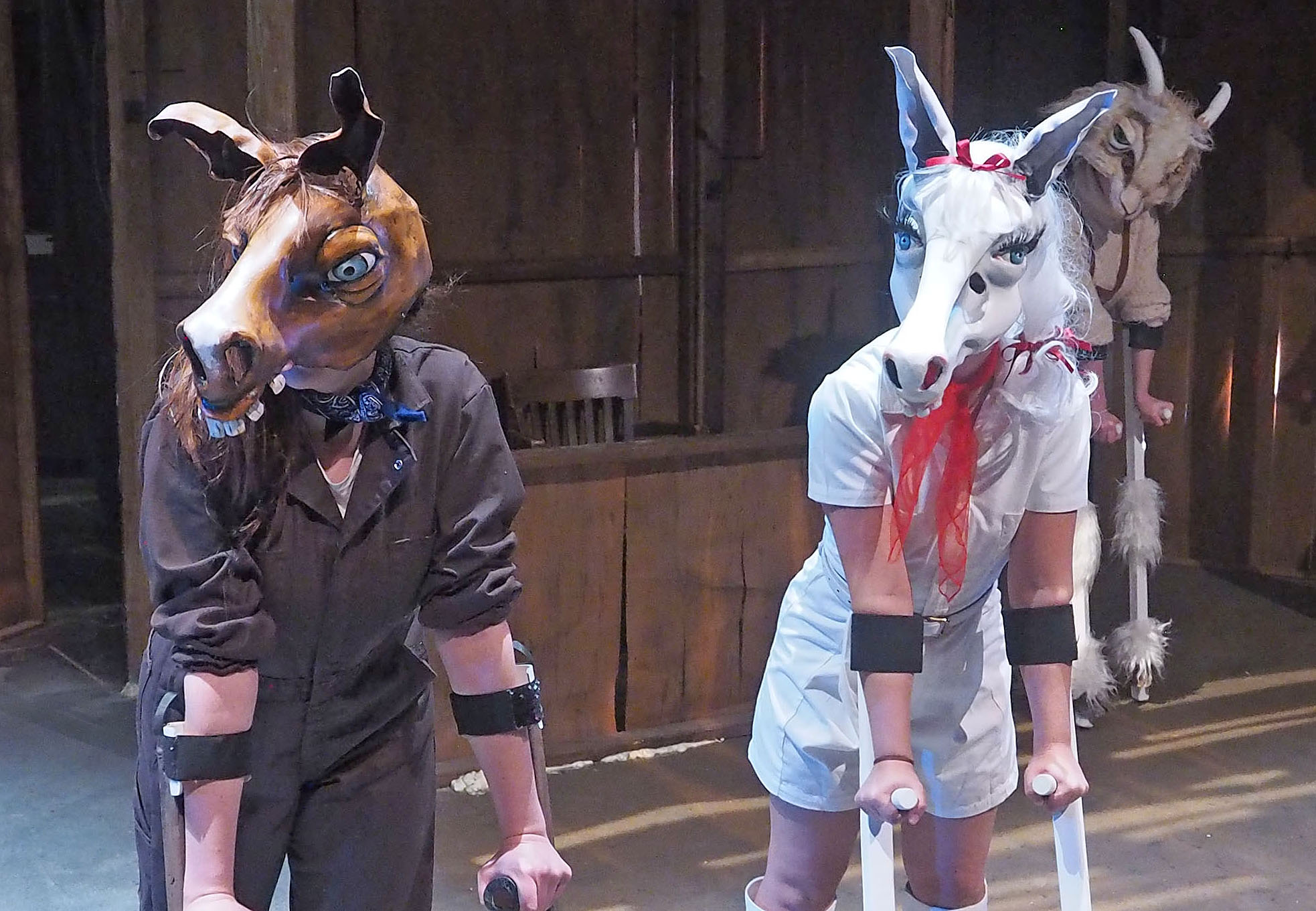 Two performers in large horse masks. They lean on crutches as they look outward. 