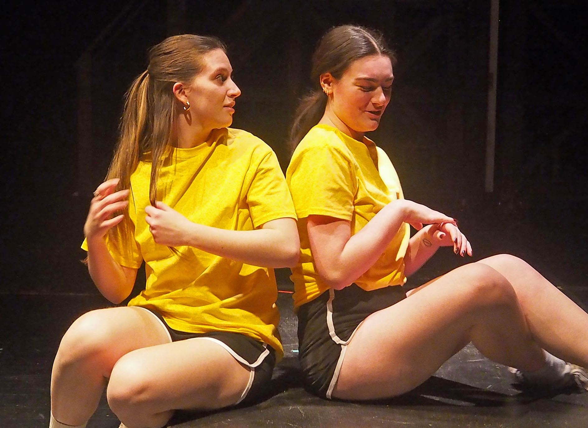 Two young women wearing matching yellow gym uniforms, sitting. 
