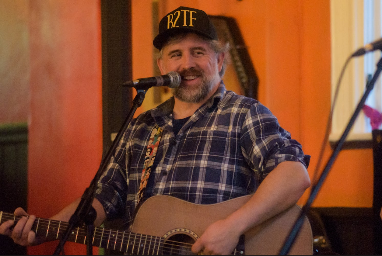 A man in a plaid shirt playing the acoustic guitar.