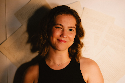 Headshot of Alina Siwy. She wears a black top and smiles at the camera. Her shadow is seen on a white backdrop. The image is from the shoulders up. 